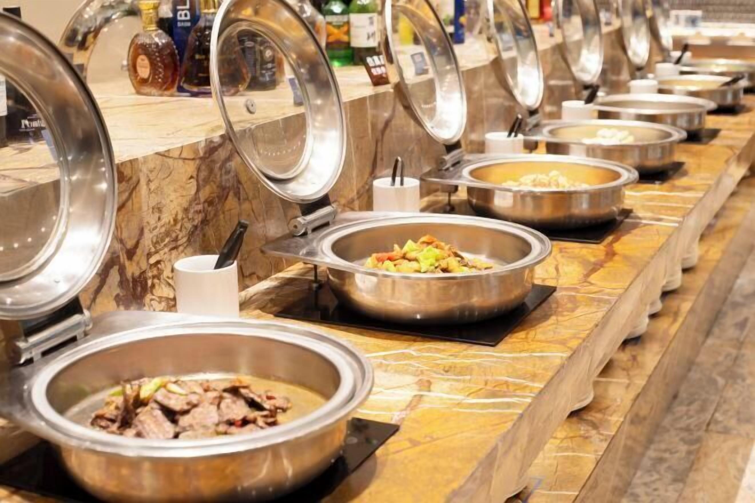 Una barra de buffet con diversas opciones de comida, incluyendo un plato de carne, un plato de verduras y una sopa cremosa.