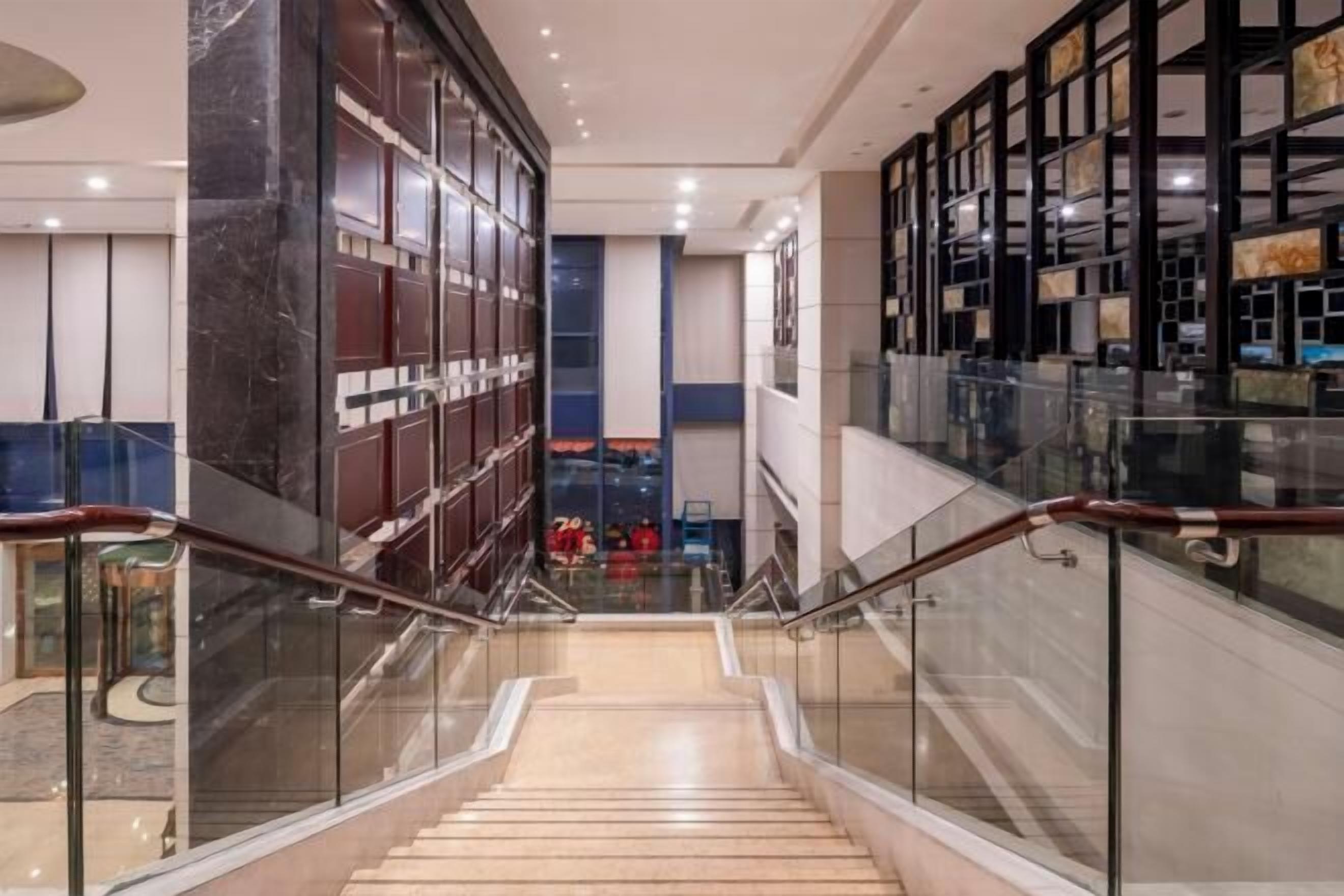 A modern interior with a glass railing staircase, marble flooring, and a view of a retail store in the background.