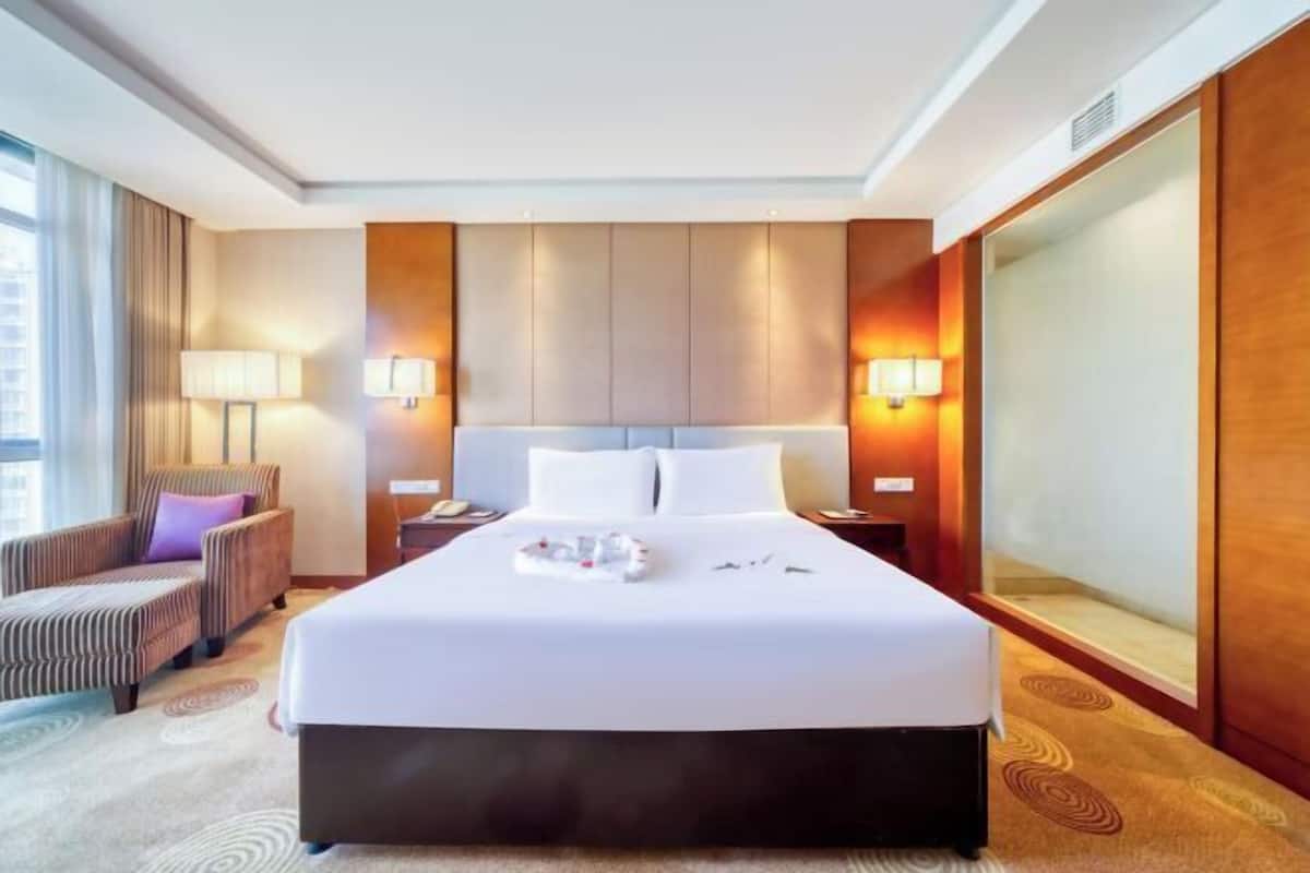 Een hotelkamer met een groot bed, twee nachtkastjes, een stoel en een groot raam.
