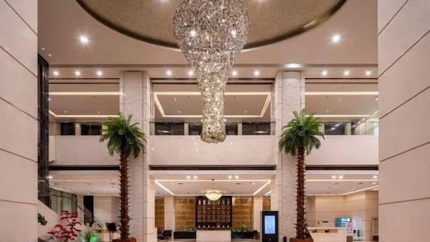 Eine geräumige Lobby mit einem großen Kronleuchter, Palmen und einer Rezeption.