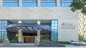 Ein moderner Hotelzugang mit einer gewölbten Glasüberdachung, Steinlöwenstatuen und einer Ziegelhausfassade.