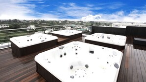 Eine Dachterrasse mit drei Whirlpools auf einer Holzterrasse, mit Blick auf eine Stadtlandschaft.