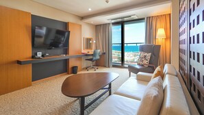 Ein Hotelzimmer mit großem Fernseher, einer Sitzecke, einem Schreibtisch und Blick aufs Meer.