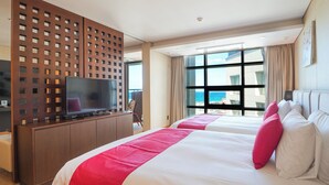 Ein Hotelzimmer mit einem großen Bett, einem Fernseher auf einer Holzkabine und Blick auf die Stadt durch große Fenster.