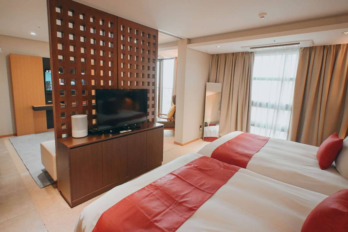 Une chambre d’hôtel avec un grand lit, un téléviseur posé sur une commode en bois, un bureau et une vue sur l’extérieur.