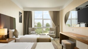 Une chambre d’hôtel avec deux lits, un bureau, une télévision et une grande fenêtre donnant sur la ville.