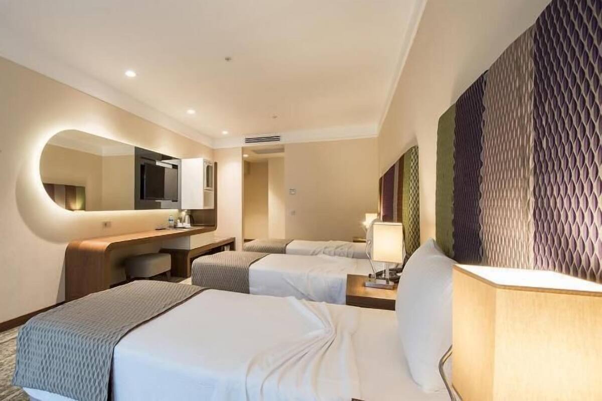 Quarto de hotel com duas camas, uma mesa, um espelho e televisão na parede.