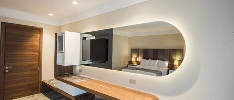 Una habitación de hotel moderna con un banco de madera, un espejo grande, un televisor de pantalla plana y una cama con cabecera.