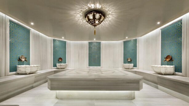 Une salle de bain spacieuse et moderne, dotée d’un grand lavabo en marbre, de vases décoratifs et d’un luminaire au plafond au design original.
