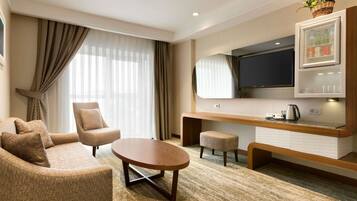 Habitación de hotel con sofá, sillón, mesa de centro, televisión y minibar.