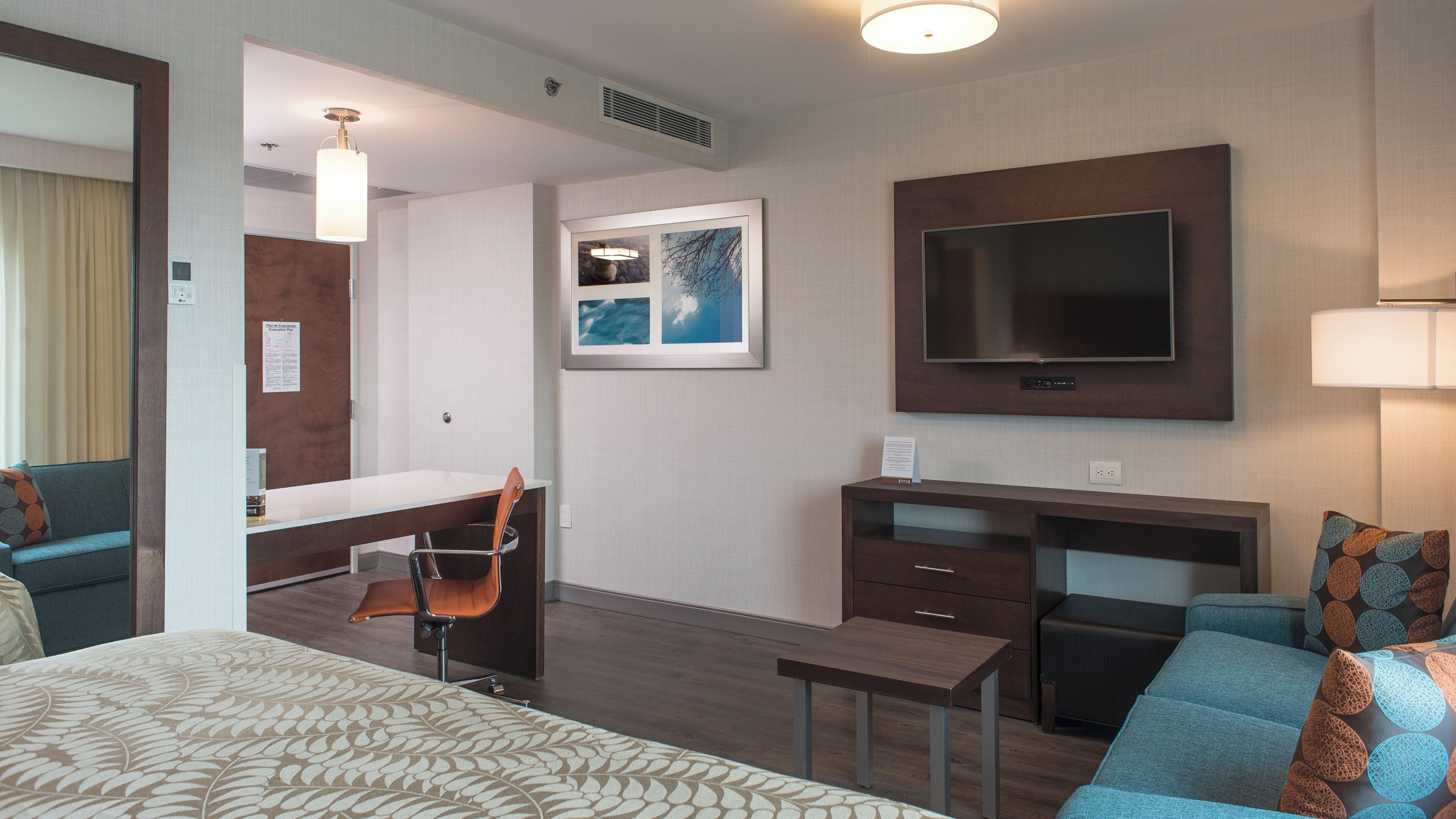 A hotel room with a bed, a desk, a TV, a chair, and a sofa.