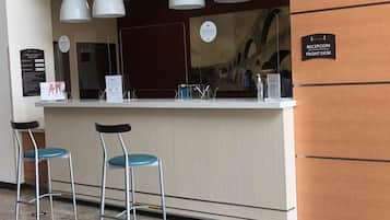 A reception desk with a sign indicating 'RECEPCIÓN FONT DESK,' two barstools with blue cushions, and a wall-mounted sign with hotel information.