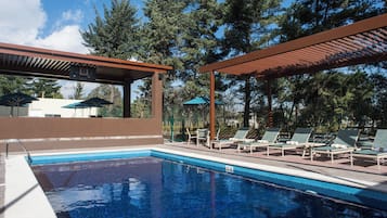 A swimming pool with lounge chairs and umbrellas, surrounded by trees.
