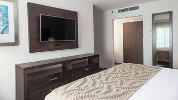 A hotel room with a flat-screen TV mounted on the wall, a dark wooden dresser with drawers, a bed with a patterned bedspread, and a wardrobe with a mirror.