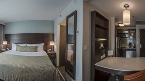 Habitación de hotel con cama, sofá, mesa de comedor, televisor y zona de cocina.