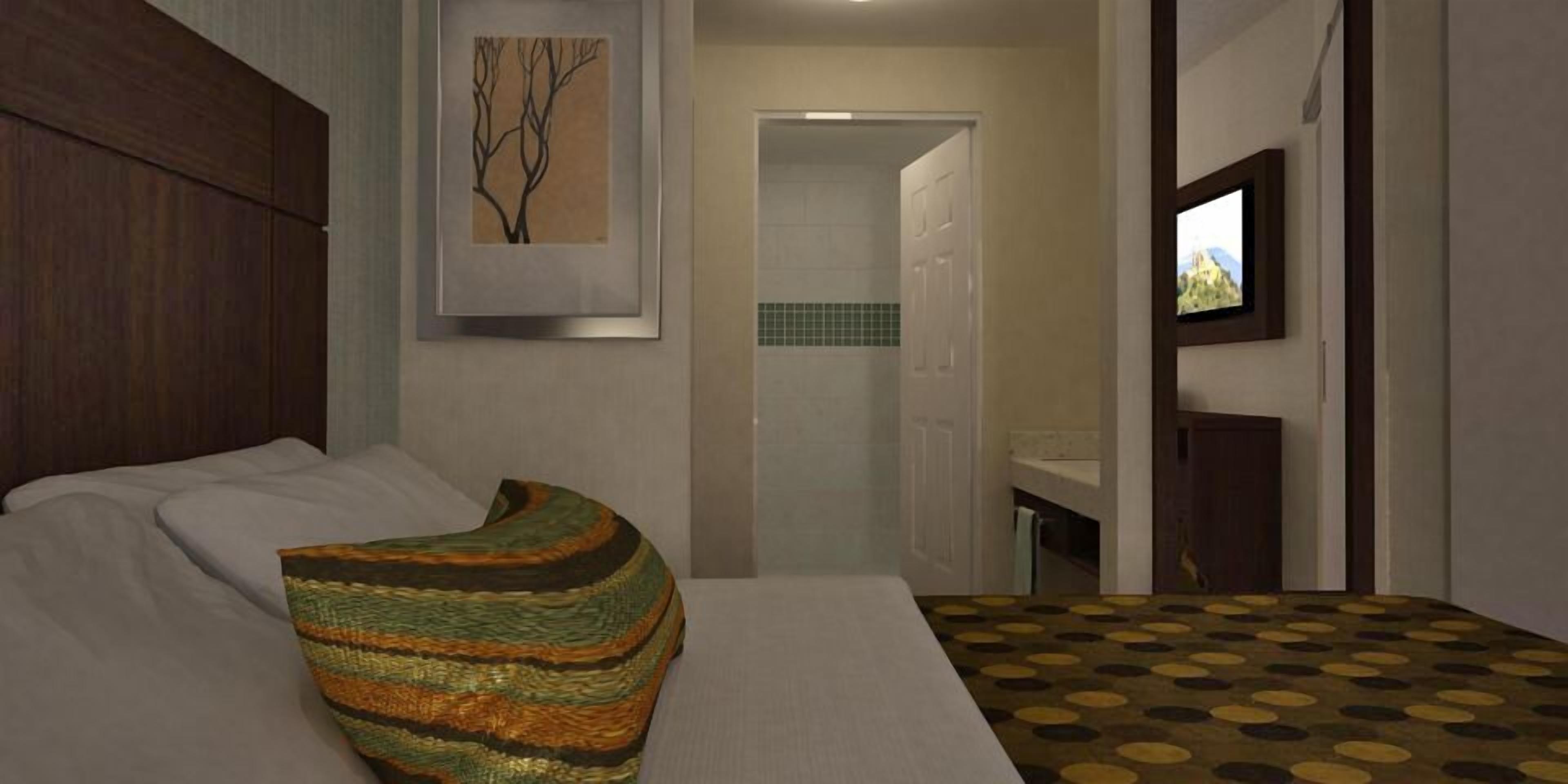 A bedroom with a bed, a pillow, a framed picture, a door, and a bathroom visible in the background.
