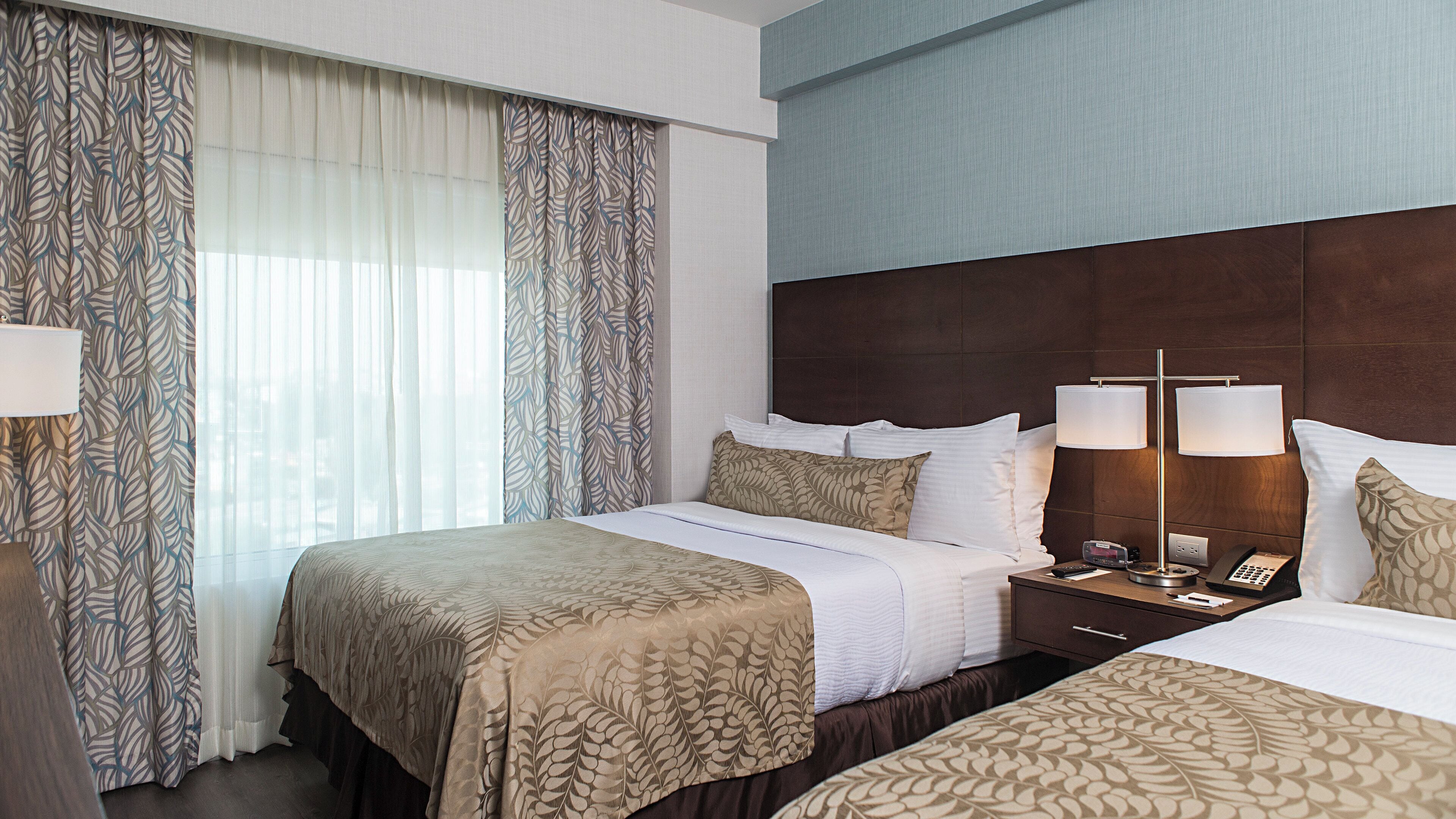 A hotel room with a large bed, bedside tables, a lamp, and curtains.