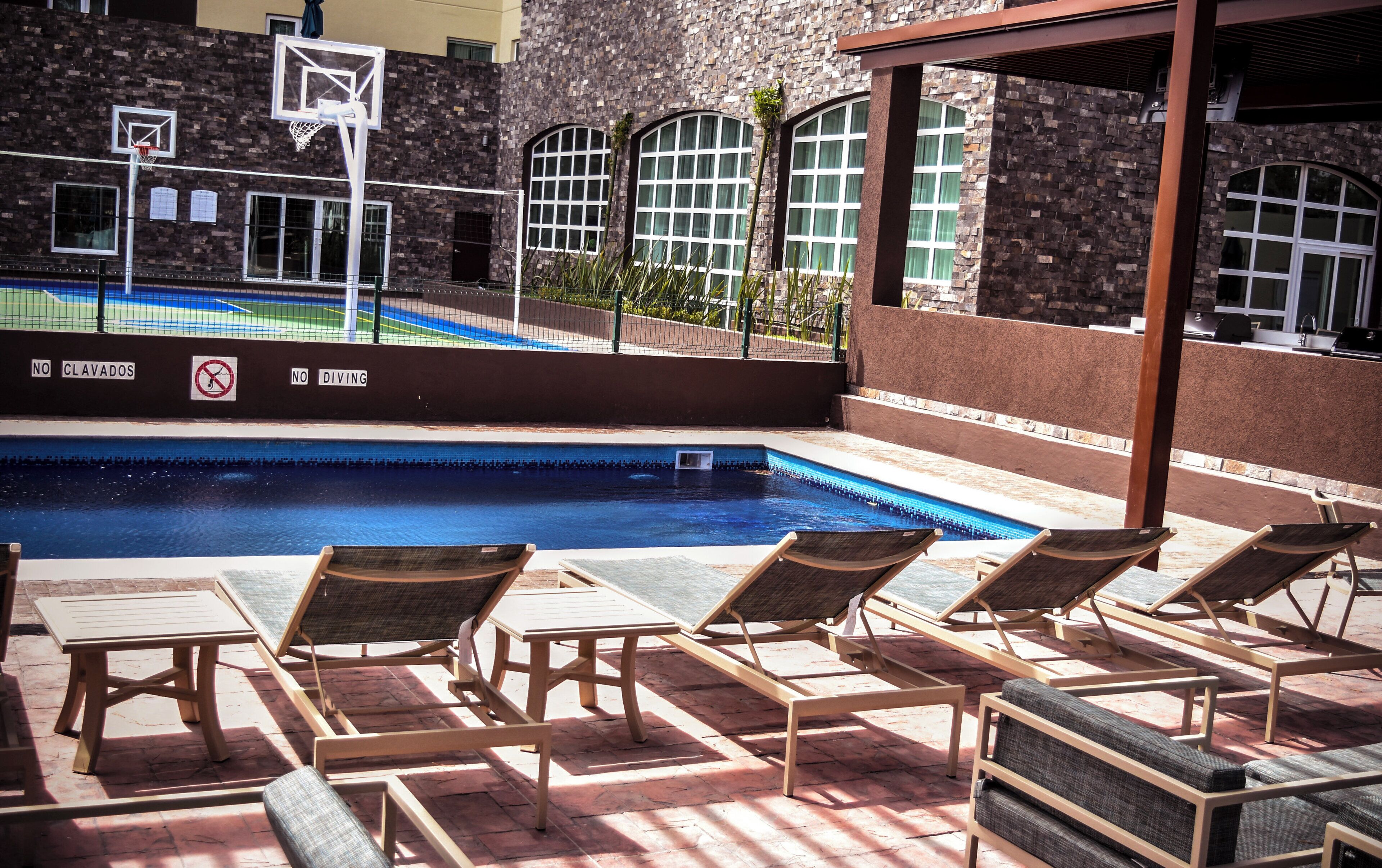 A pool area with lounge chairs and a basketball hoop.