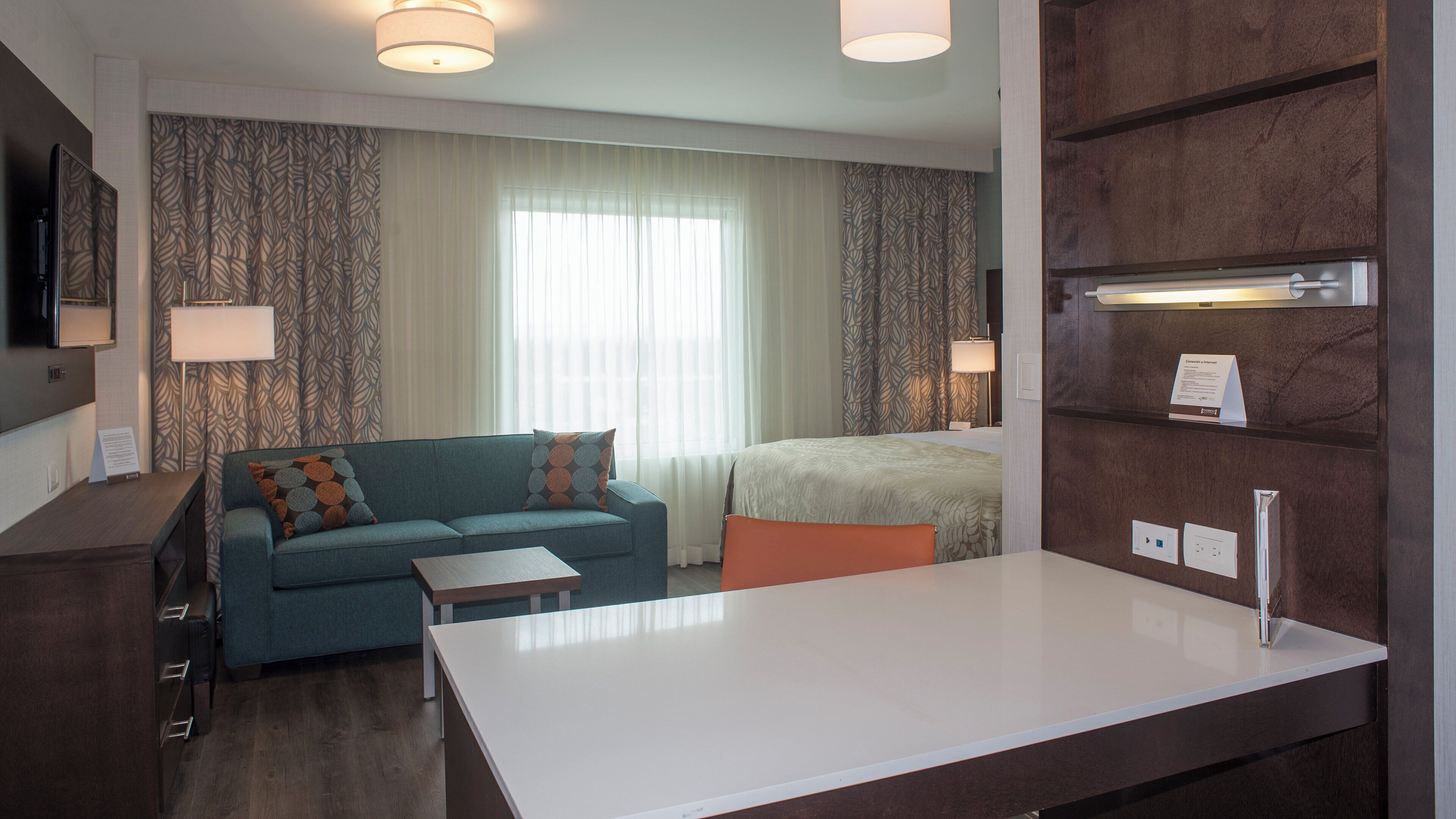 A hotel room with a sofa, a bed, a desk, and a television.