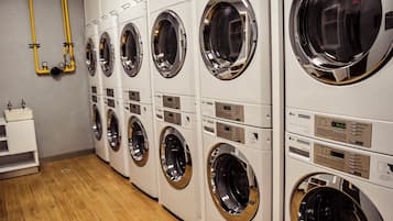 A row of white commercial washers with control panels, a wooden floor, and a small white shelf with a sink.