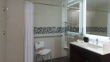 Une salle de bain moderne avec une douche à l’italienne en verre, un lavabo blanc et une petite chaise.
