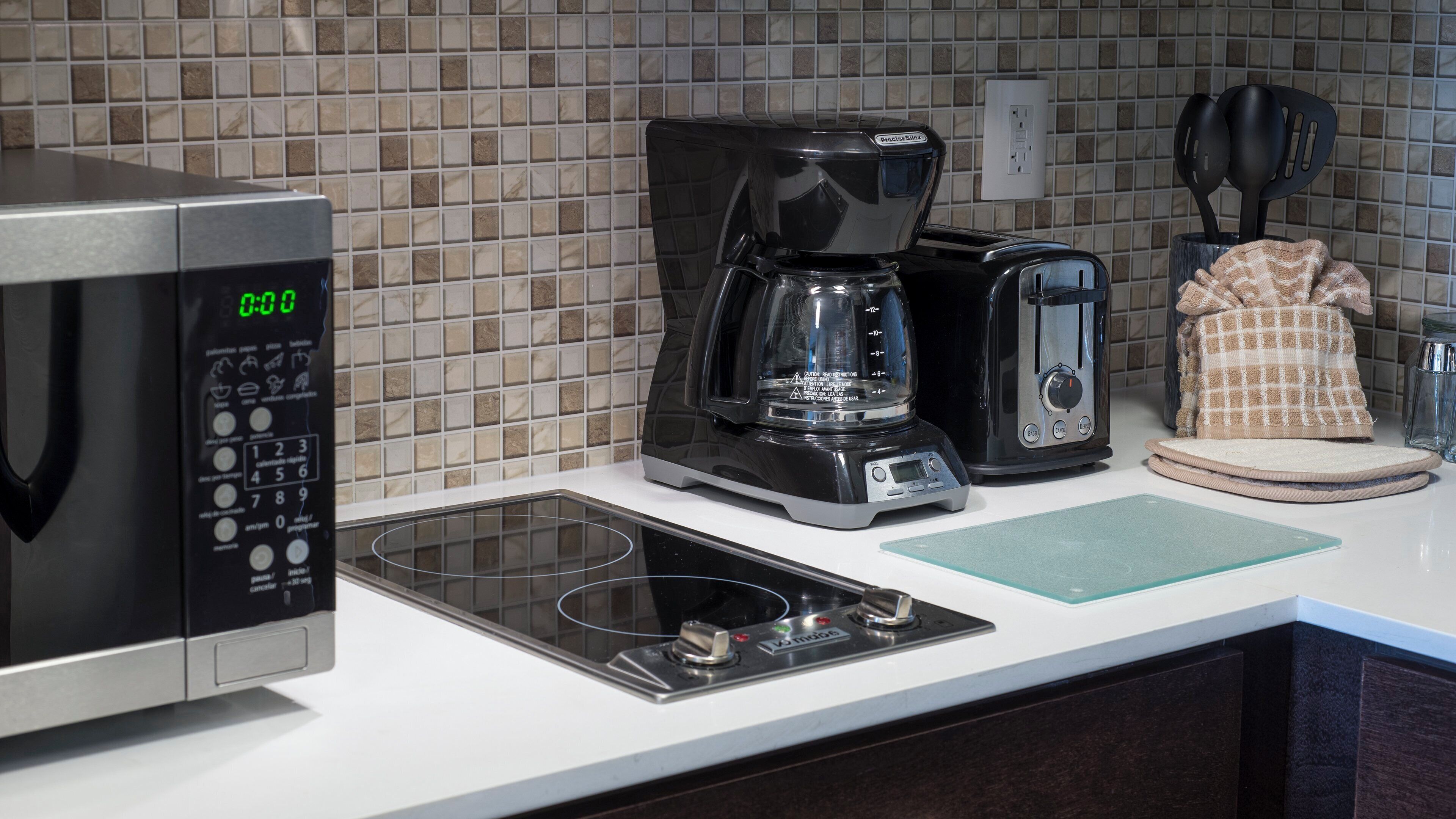 A kitchen with a microwave, coffee maker, toaster, and a digital clock.