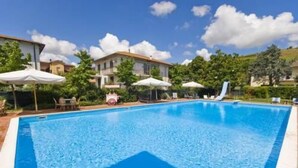 A swimming pool with lounge chairs and umbrellas, surrounded by buildings and greenery. - Hotel Giardino (San Lorenzo in Campo)