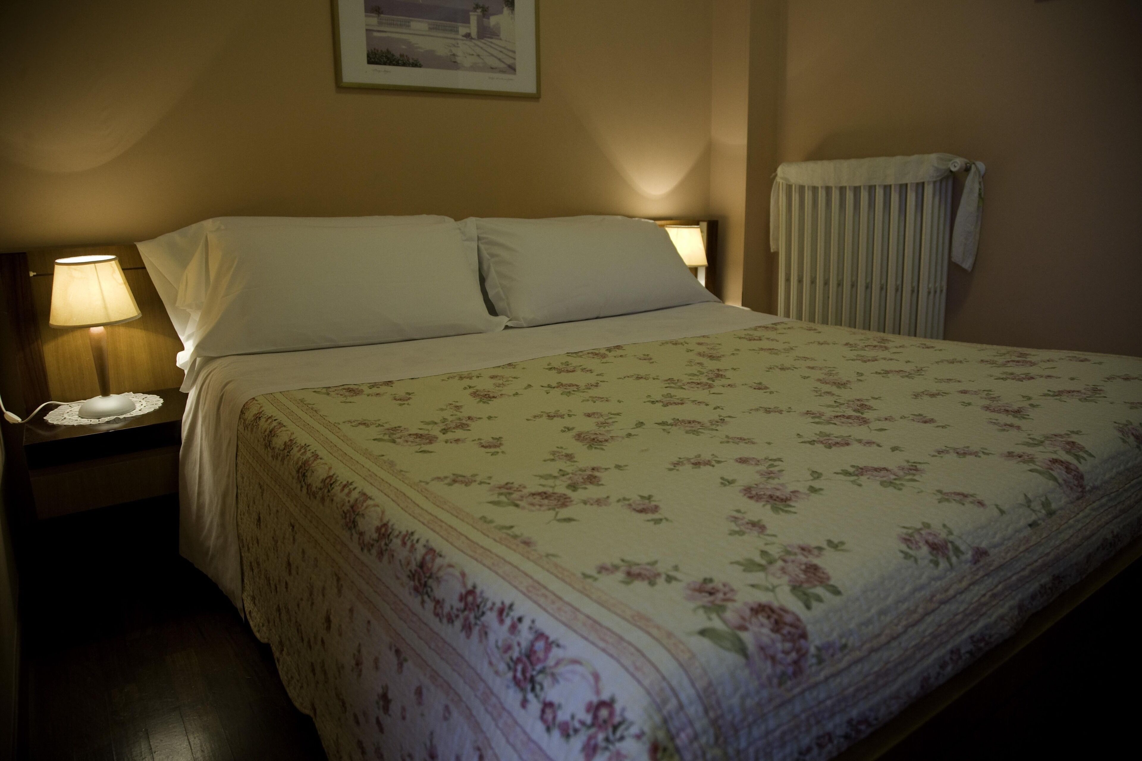 A neatly made bed with a floral bedspread, two bedside lamps, and a framed picture on the wall.