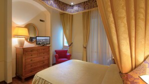 A hotel room with a bed, a wooden dresser, a red chair, a television, and curtains. - Hotel Giardino (San Lorenzo in Campo)