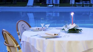 A dining table set for two with white tablecloths, two wine glasses, a candle, and a floral centerpiece. - Hotel Giardino (San Lorenzo in Campo)