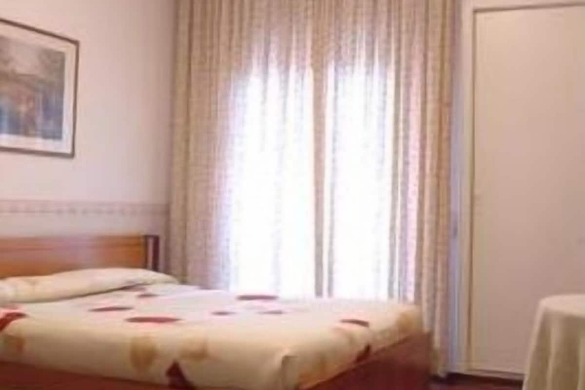 Une chambre à coucher avec un lit, un plancher en bois, une fenêtre avec des rideaux et une porte.