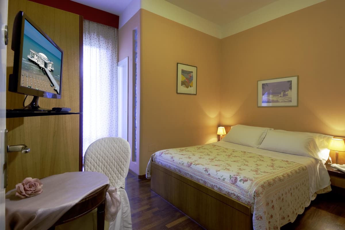 Une chambre d’hôtel avec un lit, un bureau, une chaise, une télévision et deux tableaux accrochés au mur.