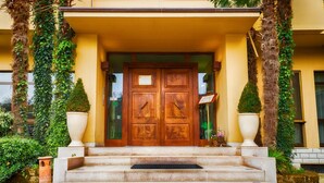 A building entrance with a wooden double door, steps leading up to it, and two large planters on either side. - Hotel Giardino (San Lorenzo in Campo)