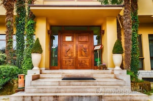 A building entrance with a wooden double door, steps leading up to it, and two large planters on either side.