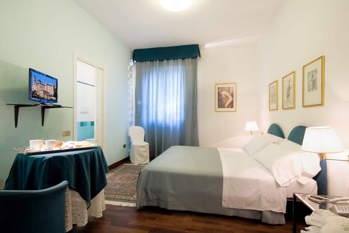 Une chambre d’hôtel avec un lit, une table de chevet, une chaise et un téléviseur posé sur un meuble.
