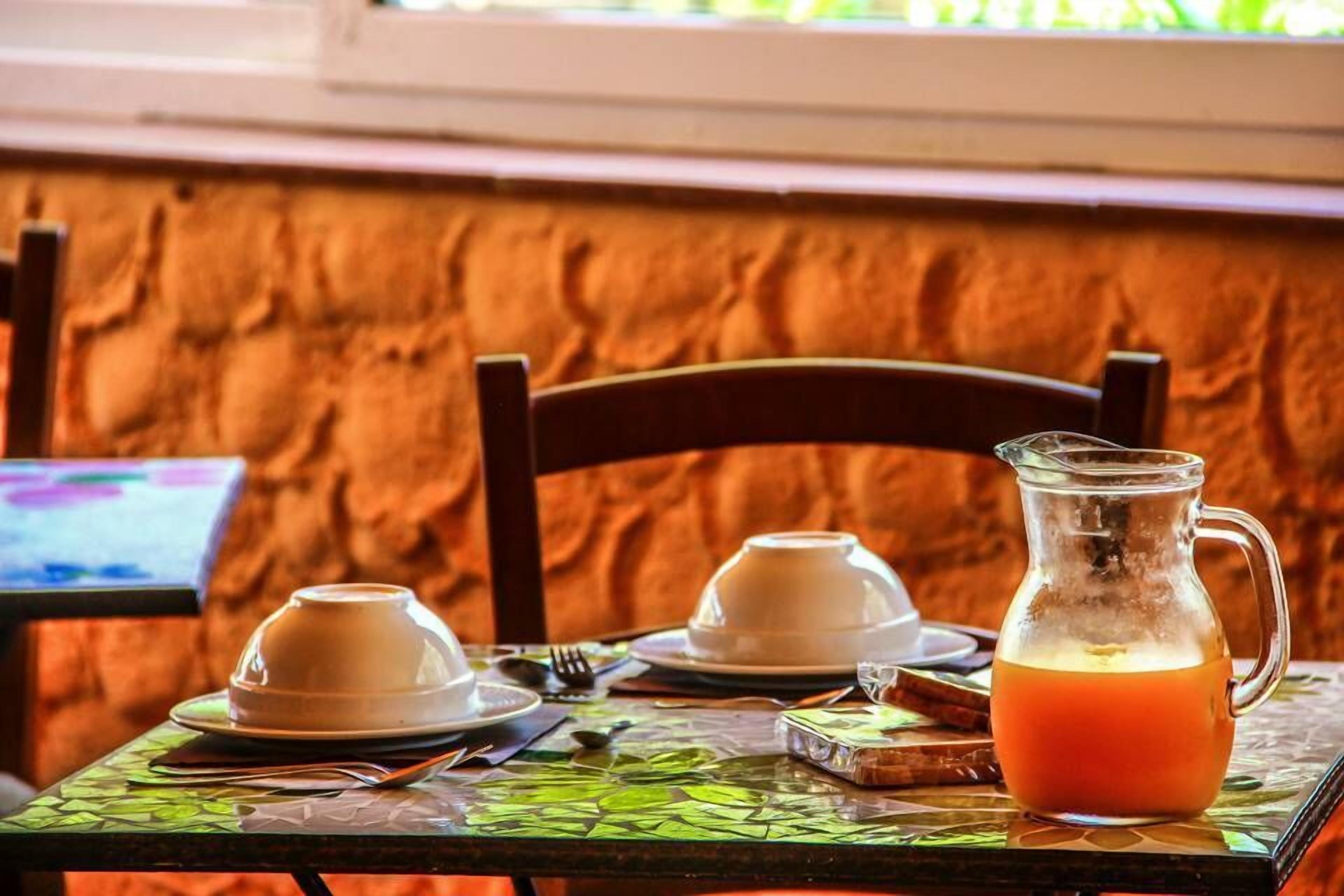 Une table avec un pichet en verre rempli de jus d’orange, deux tasses blanches et une assiette de toasts.