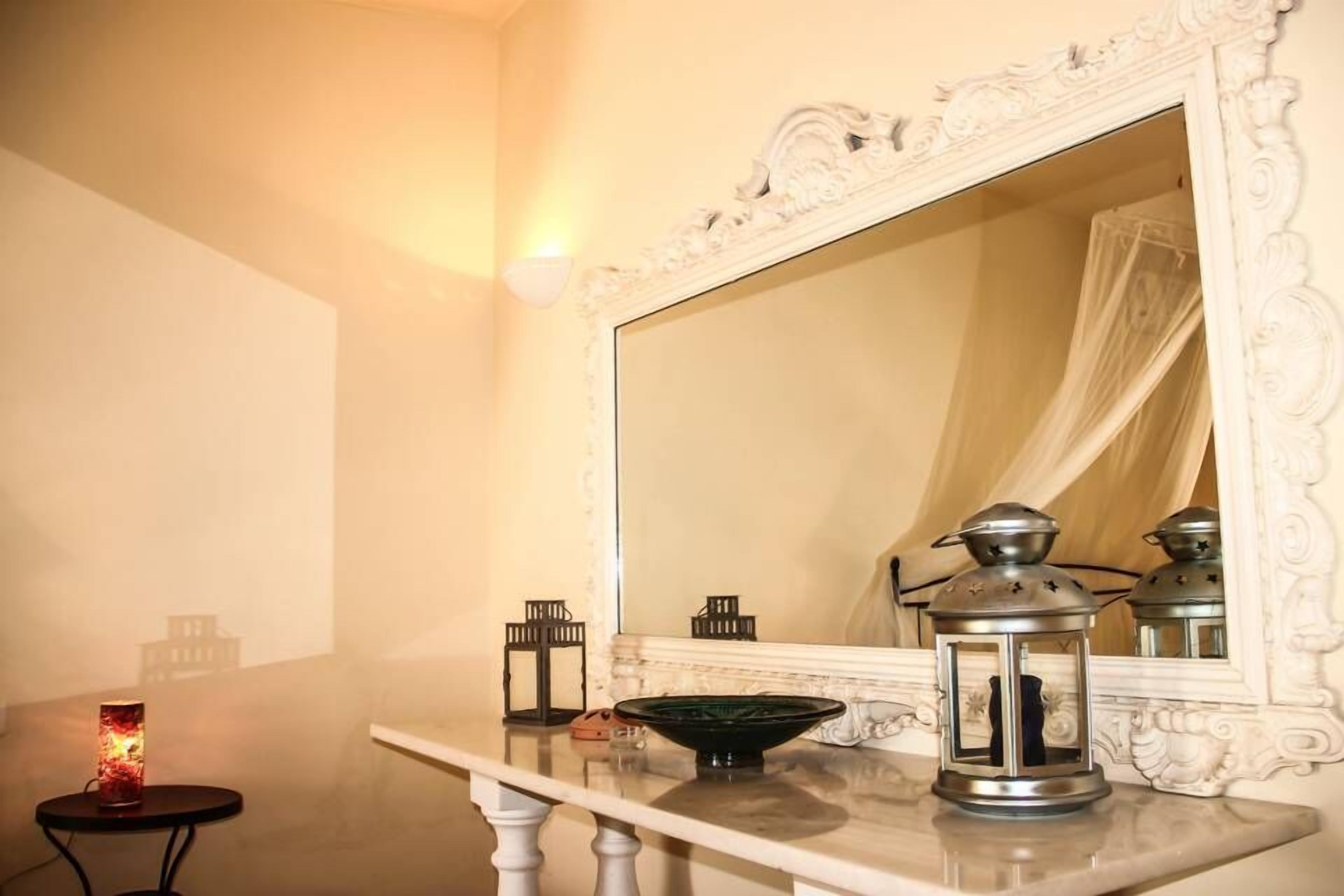A bathroom with a large mirror, a white vanity, a small table with a candle, and two lanterns.