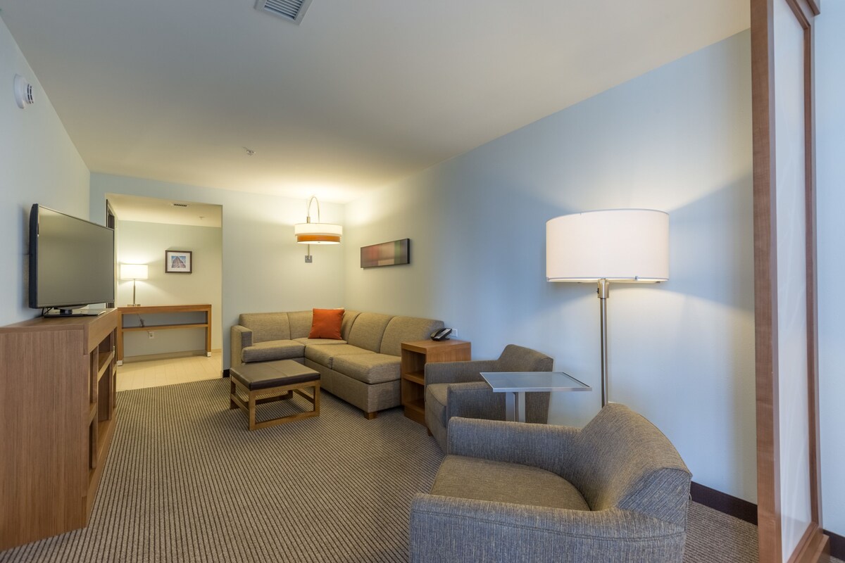 A hotel room with a flat-screen TV, a sofa, a coffee table, a lamp, and a small table.