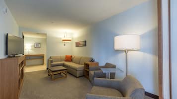 A hotel room with a flat-screen TV, a sofa, a coffee table, a lamp, and a small table.