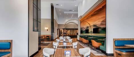 A modern dining area with long tables and chairs, a bar area, and a view of a mountainous landscape through a large window.