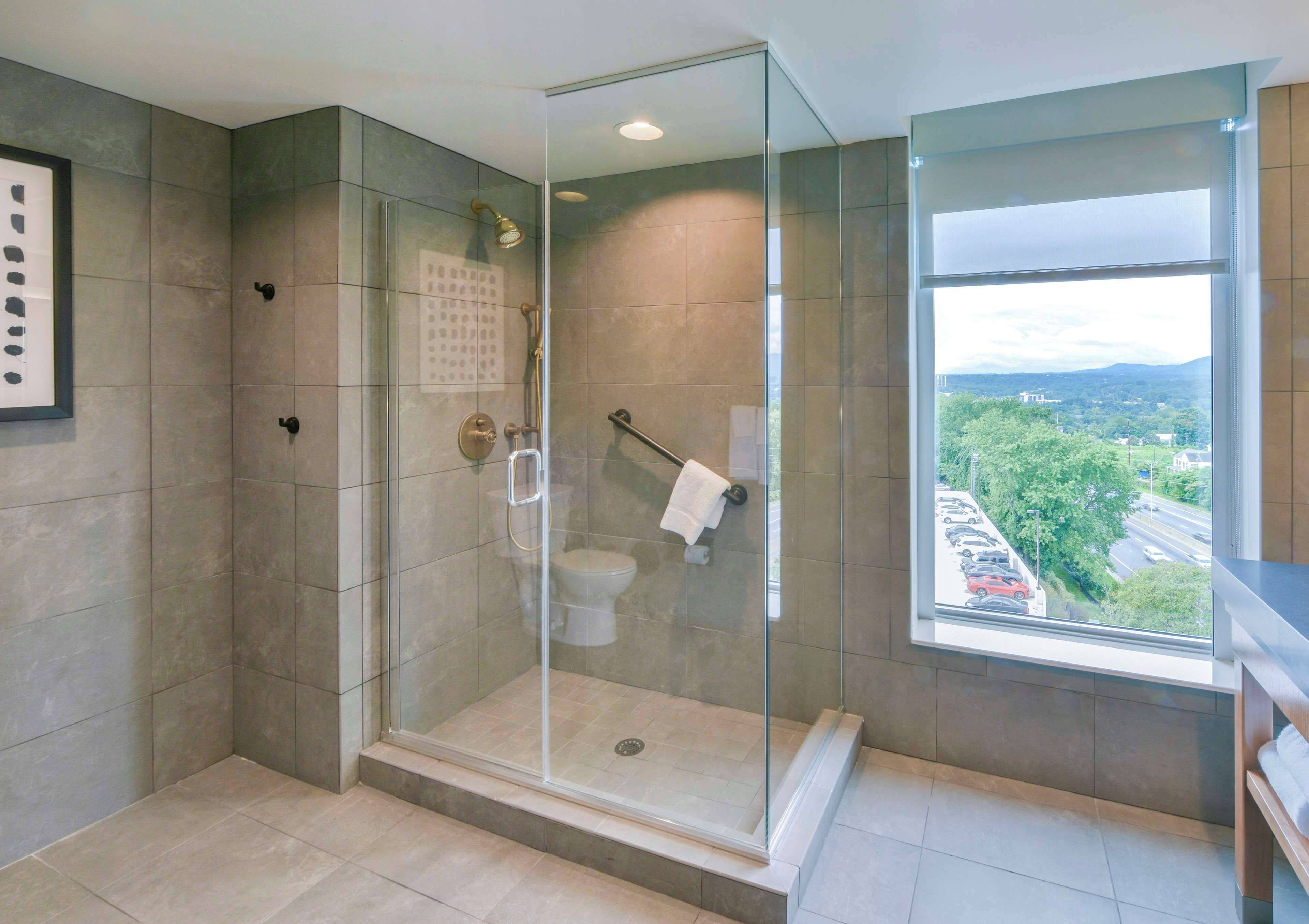 Ein modernes Badezimmer mit einer Glaskabine zur Dusche, Toilette und einem großen Fenster mit Blick nach draußen.