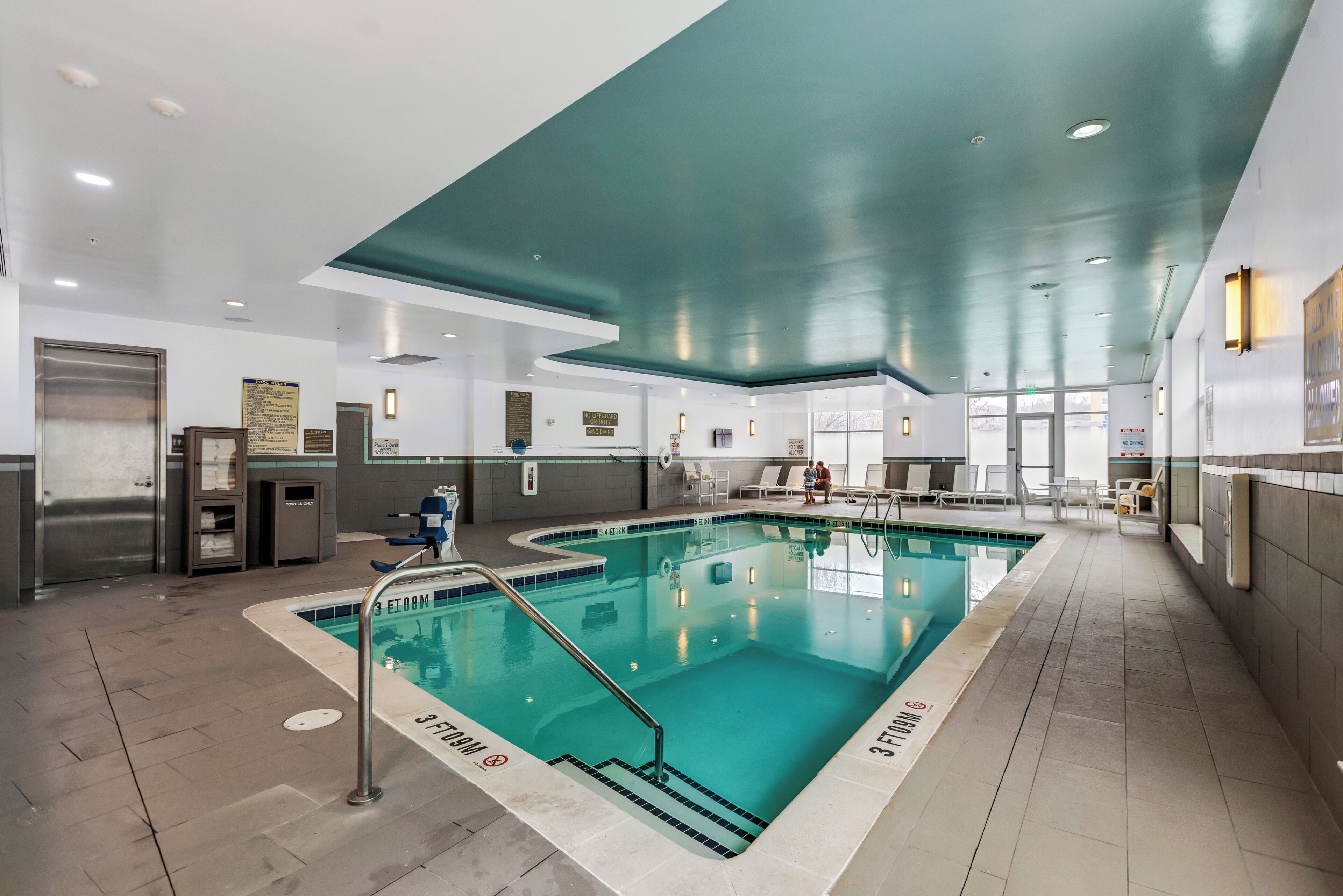 A large indoor swimming pool with clear water, surrounded by lounge chairs and a tiled floor.
