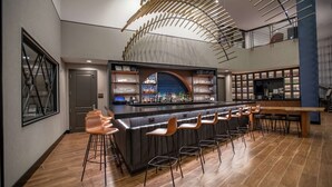 A modern bar area with a long counter, multiple stools, and a variety of bottles and glasses. - DoubleTree by Hilton Asheville Downtown (Asheville)