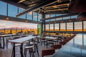 Une salle à manger spacieuse avec de hauts plafonds, de grandes fenêtres et une vue sur un paysage montagneux.