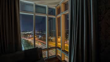 Ein Zimmer mit großem Fenster mit Blick auf eine nächtliche Skyline, ausgestattet mit modernem Interieur, einer Couch und Vorhängen.