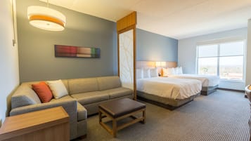 A hotel room with a sofa, a bed, a small table, and a window with a view.