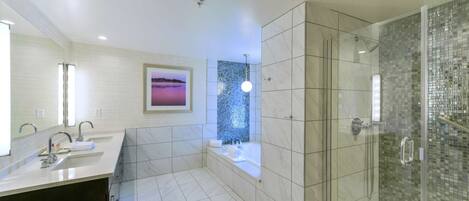 A modern bathroom with a large mirror, two sinks, a bathtub, and a glass-enclosed shower.