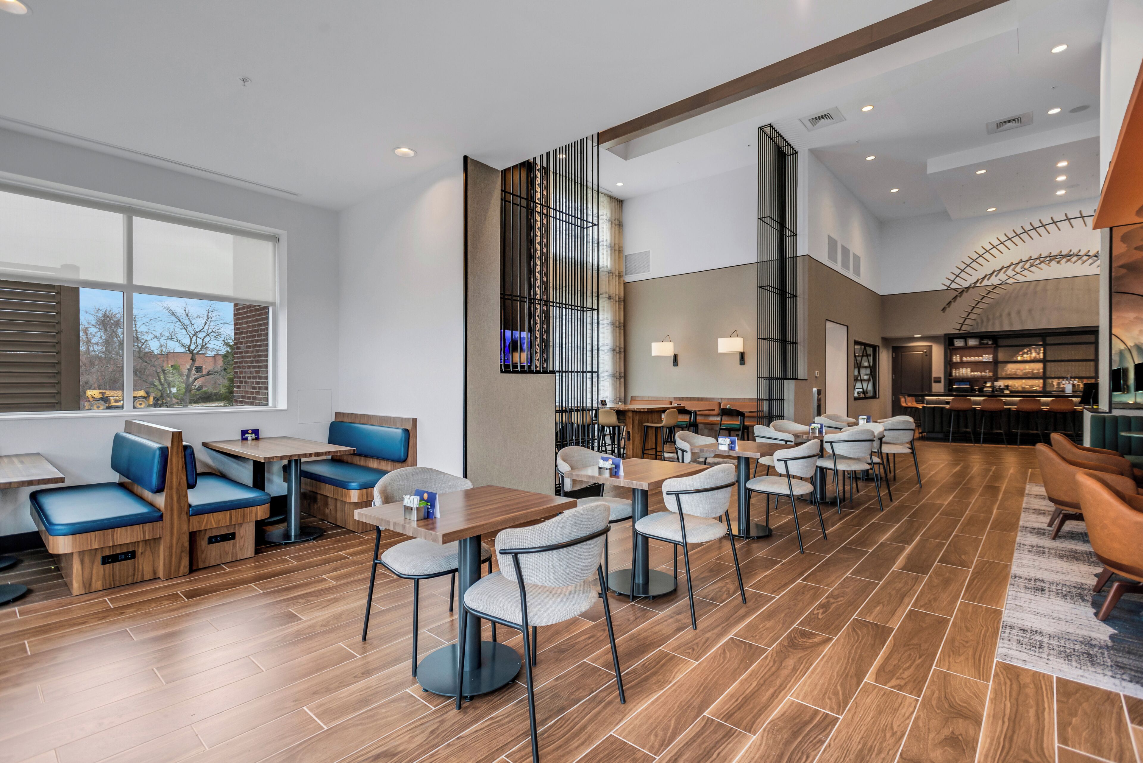 A modern restaurant with high tables and booths, a bar area, and a view of the outdoors.