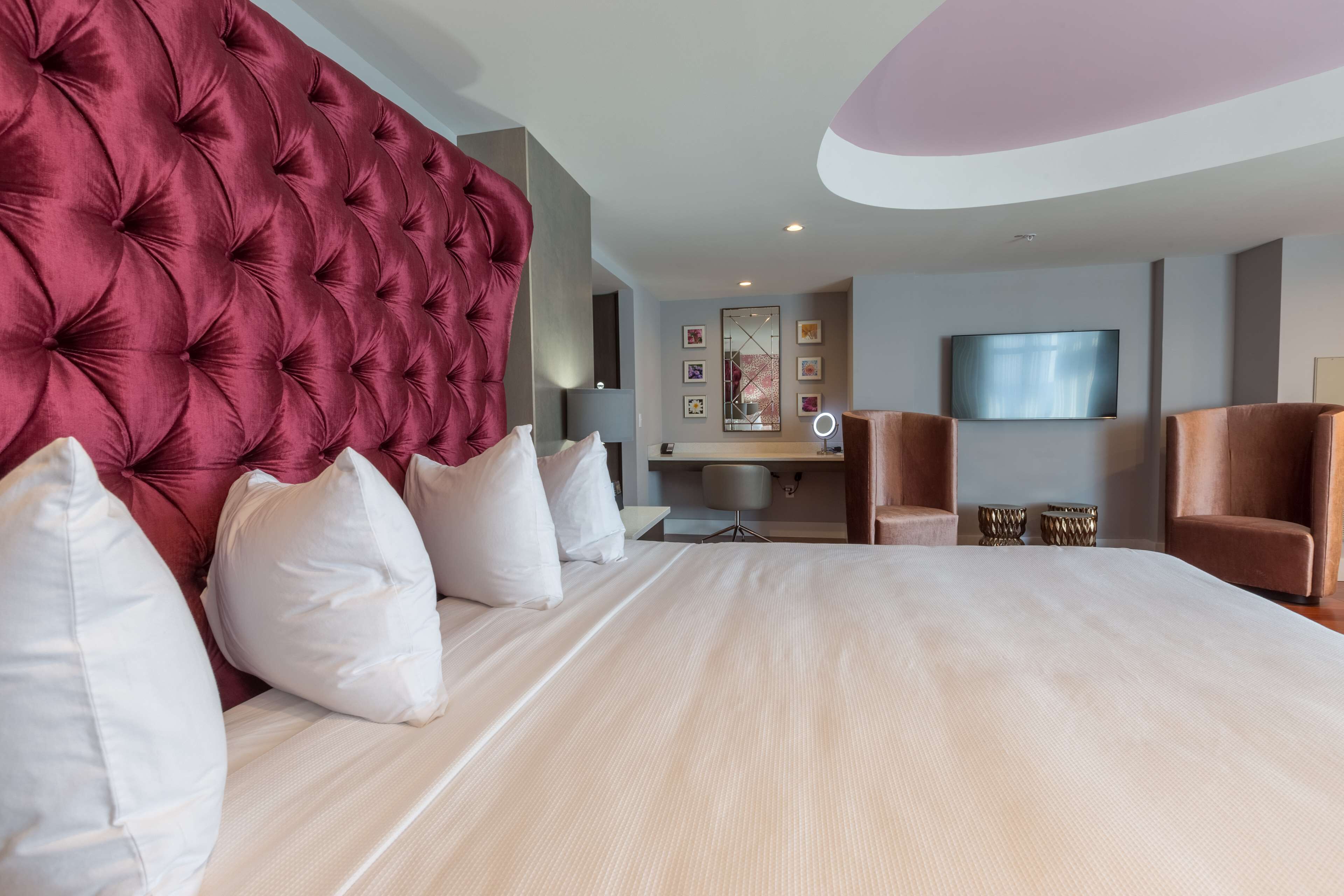 Habitación de hotel con una cama grande, cabecero capitonado, escritorio, una silla y televisor.