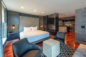 A modern hotel room with a large bed, two armchairs, a small table, and a TV.